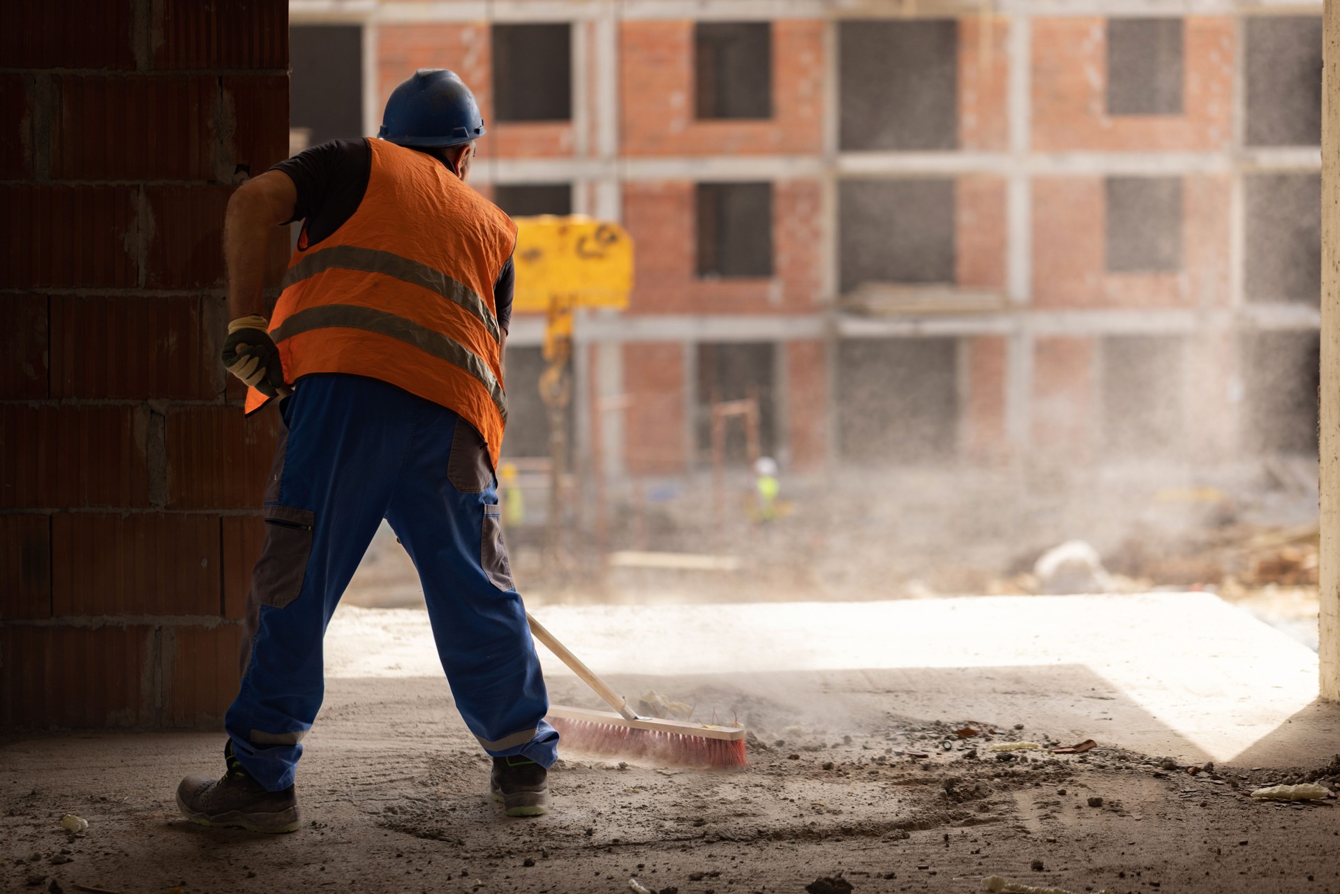 Rear-view of unrecognizable construction worker using broom to clean the dust on construction site